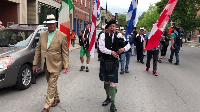 Un joueur de cornemuse suivi de marcheurs portant les drapeaux de l'Irlande, de Montréal, du Québec et du Canada.