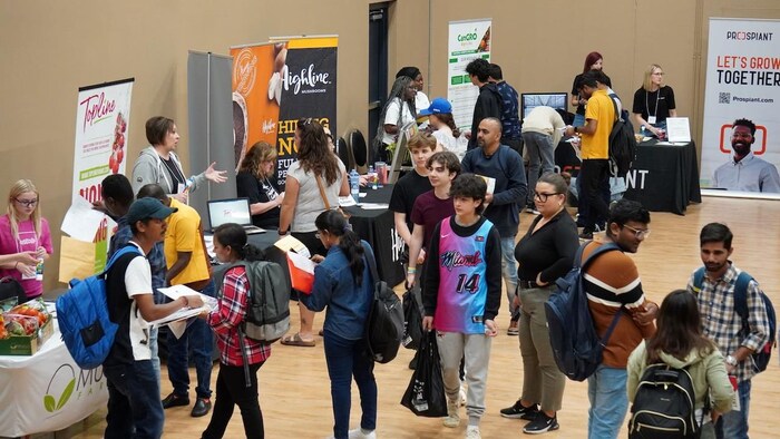 Des jeunes sont dans une salle où des employeurs tiennent des kiosques d'informations et de recrutement.
