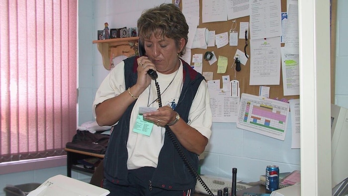 Une femme debout dans un bureau, au téléphone. Elle tient une carte.