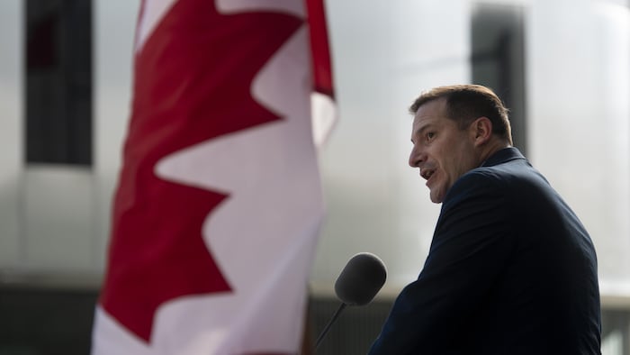 Un homme parle au micro à côté d'un drapeau canadien.