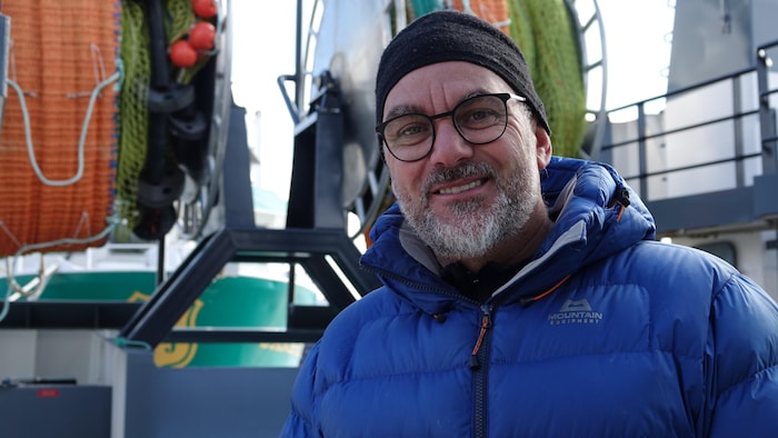 Marco Turbide, un homme avec des lunettes et une barbe, se tient souriant devant un bateau.