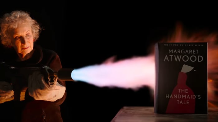 L'autrice tient un lance-flammes en direction d'un livre posé sur une table. 