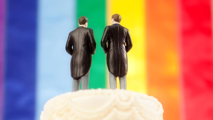 Figurines représentant deux hommes au sommet d'un gâteau de mariage, devant un drapeau arc-en-ciel.