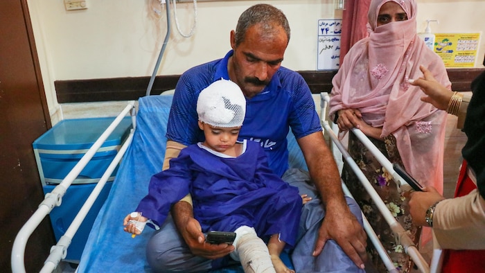 Un homme et un enfant qui porte des bandages à la tête et un plâtre à la jambe droite dans un lit d'hôpital.