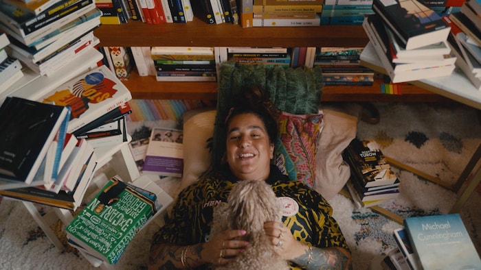 Mariana Mazza sourit allongée au sol avec son chien, entourée de livres.