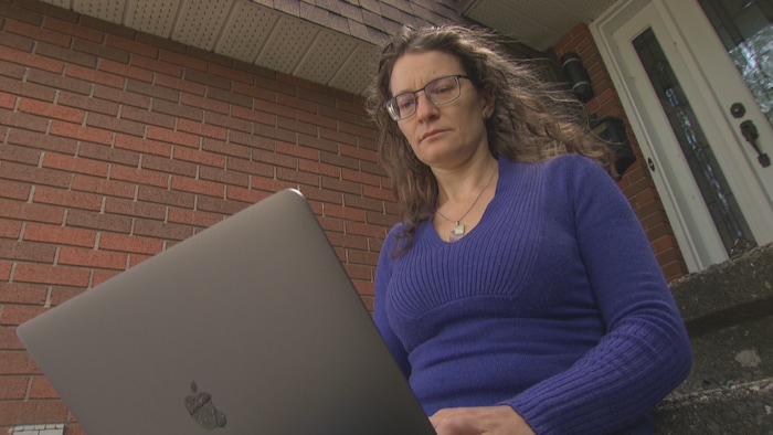 Marianne Ariganello devant son ordinateur portatif, assise devant l'entrée de sa maison.