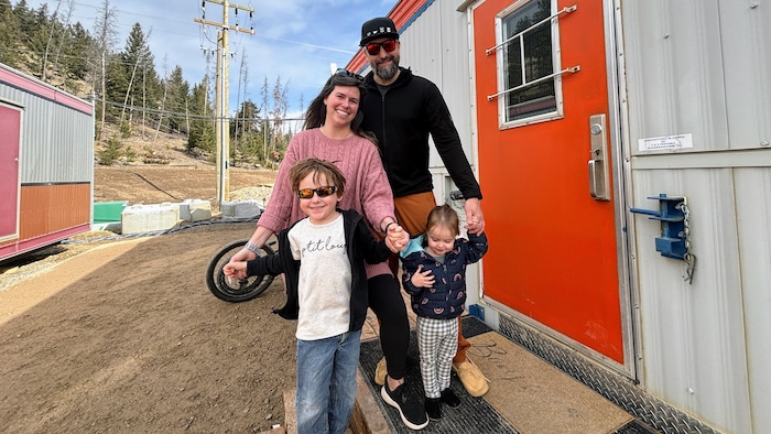 Une femme, son mari et leurs deux enfants prennent la pose devant une maison mobile. 
