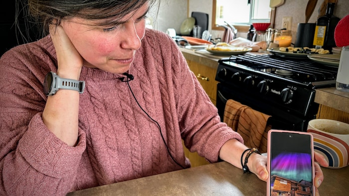Une femme montre une photo de sa maison sur son cellulaire.