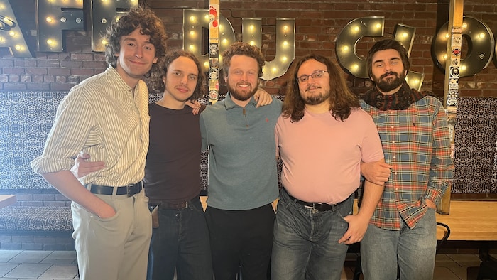 Cinq musiciens se tiennent en rang.