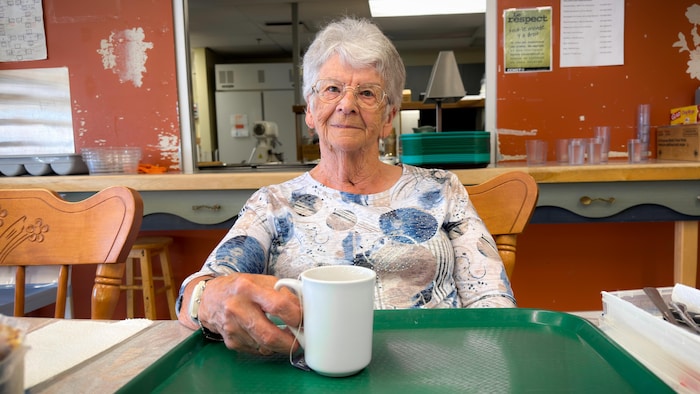 Une femme assise à une table tient une tasse de thé. 