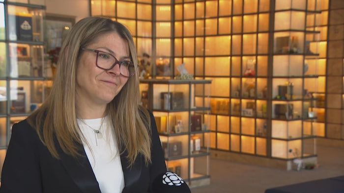 Marie Eve Garneau en entrevue avec Radio-Canada. Elle est dans un colombarium. Derrière elle, des urnes funéraires sont disposées dans des murs pour les recevoir.