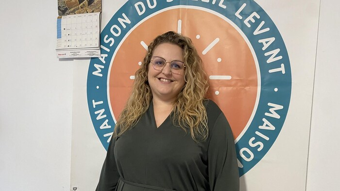 Marie-Ève Giroux debout pour se faire prendre en photo et derrière elle une affiche sur laquelle est écrit Maison Soleil levant.  