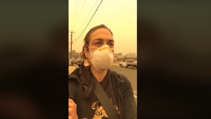 Une femme avec un masque alors que les particules de fumée de feux de forêt sont très visibles autour d'elle.