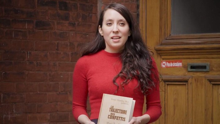L'autrice tient son livre devant la porte de son appartement.