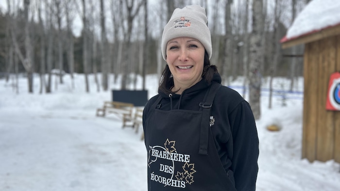 Une femme souriante porte un bonnet floqué au nom de l'érablière, dehors, dans la neige.