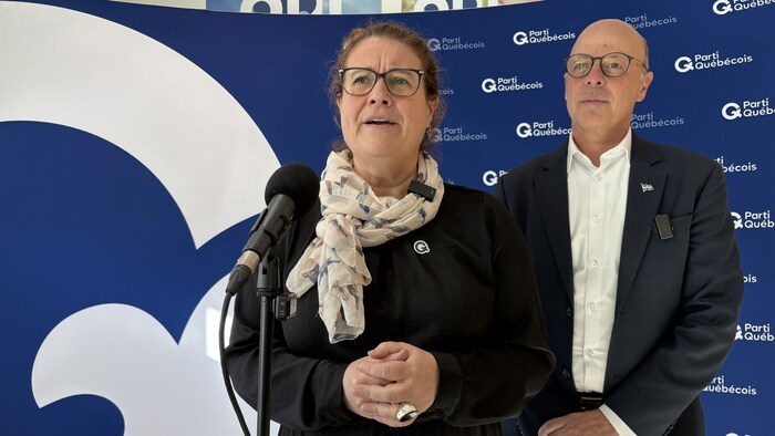 Une femme et un homme devant un micro. Une bannière aux couleurs du Parti québécois est visible derrière.