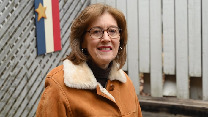 Marie-Linda Lord pose pour la photo à l'extérieur. Une décoration en bois aux couleurs du drapeau acadien derrière elle. 