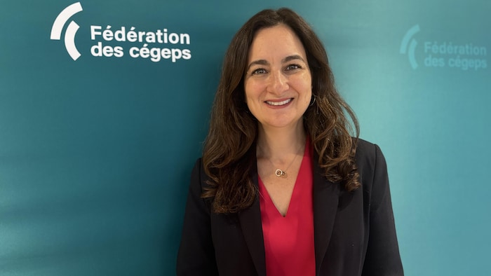 La présidente de la Fédération des cégeps souriante, posant devant le logo de la fédération.