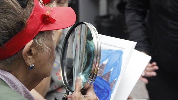 Une femme tient une loupe pour lire un texte.