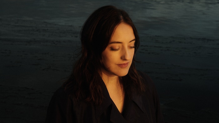 Photo de l'artiste les yeux semi-fermés devant des nuages dans l'obscurité.