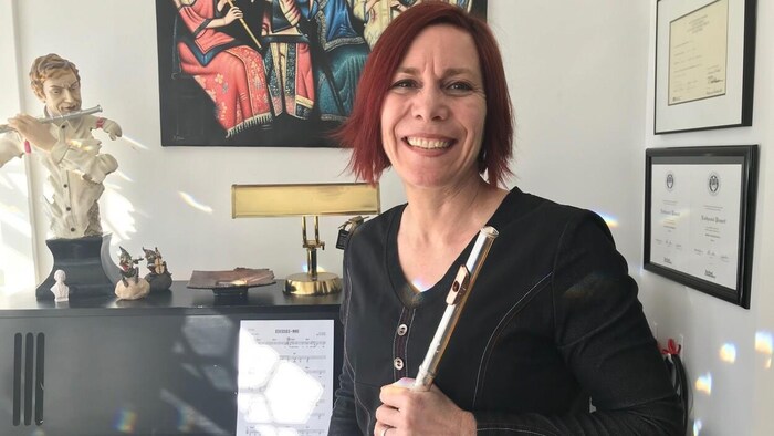 Une femme regarde la caméra en souriant devant un piano.