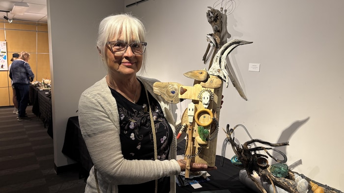 Marielle Vanasse tient une de ses sculptures de format moyen, l'exposant fièrement devant le mur de la salle.