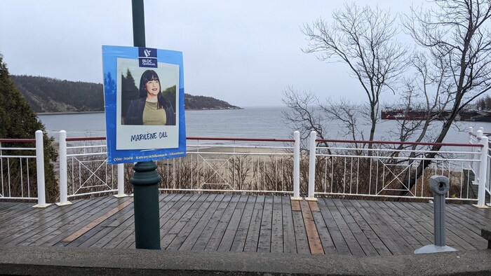 Une pancarte électorale sur un poteau devant un paysage de bord de fleuve.