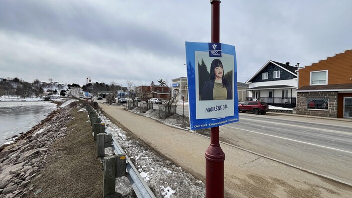Une pancarte électorale fixée sur un poteau électrique au bord d'une rue où passe une voiture