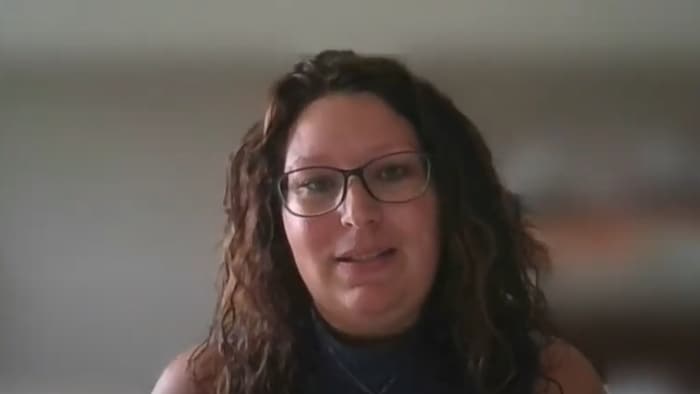 Une femme portant des lunettes se tient devant son ordinateur.
