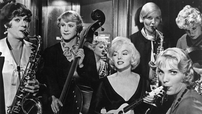 Une femme blonde joue de la guitare au milieu d'autres personnes. 
