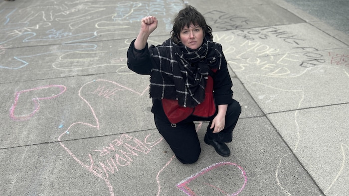Marina Classen lève le point dans les airs sur un trottoir où l’on voit le contours de corps tracé à la craie.