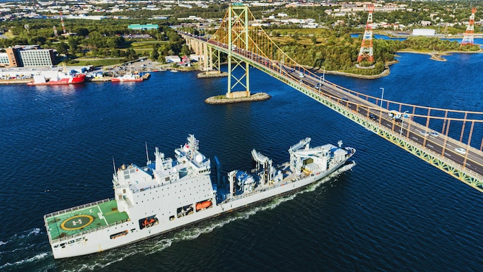Par une claire journée d'été, un navire militaire s'approche du pont. On voit la rive de Dartmouth.