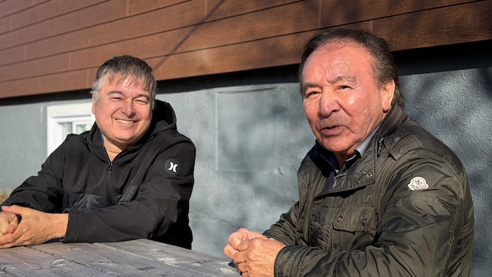 Mario Jourdain et Louis-Georges Fontaine sont assis à une table, dehors.