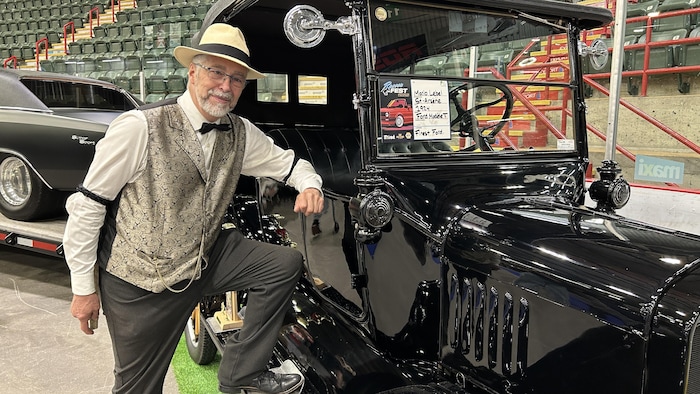 Un monsieur se tient à côté de sa voiture en souriant.