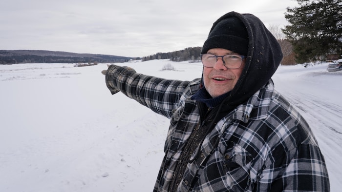 Un homme avec un manteau d'hiver pointe une forêt avec son doigt à l'extérieur.