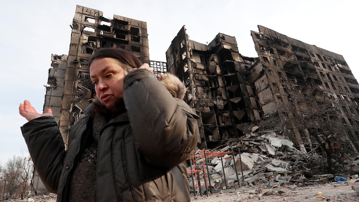 Une femme devant ce qu'il reste de tours d'habitation. Les immeubles sont éventrés et carbonisés.