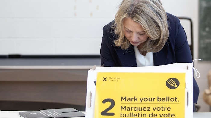 Elle est derrière un isoloir et remplit son bulletin de vote.