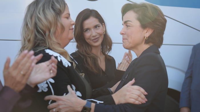 Marjolaine Ferron regarde Christine Fréchette enlacer chaleureusement une autre femme sous les applaudissements d'un groupe.