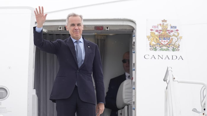Mark Carney benignant et envoie la main à l'entrée d'un avion.