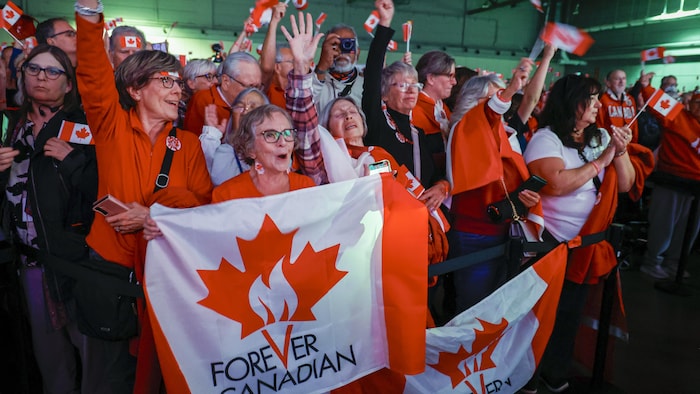 Des personnes tiennent des drapeaux canadiens.