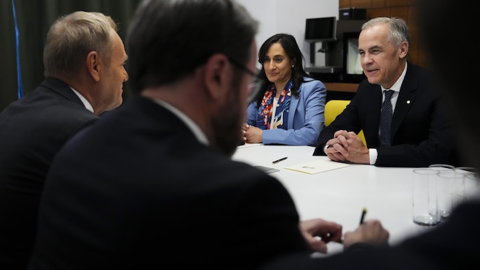 Mark Carney, Anita Anand et Donald Tusk discutent, assis à une table.