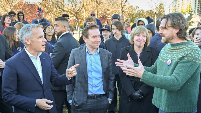 Le premier ministre canadien Mark Carney parle à un militant associatif, entouré d'une foule dans un parc à Calgary.