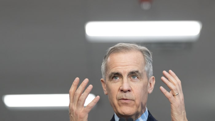 Le cook libéral Mark Carney parle au micro en gesticulant avec ses mains.