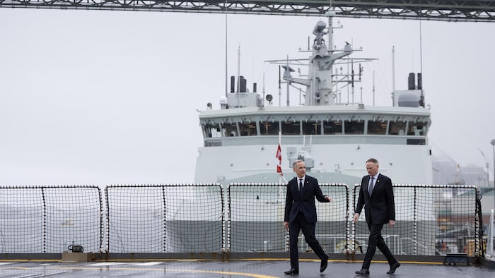 Mark Carney et David McGuinty marchent devant un grand navire de patrouille sur un port.