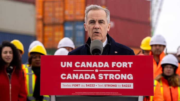 Mark Carney devant des conteneurs sur un quai.