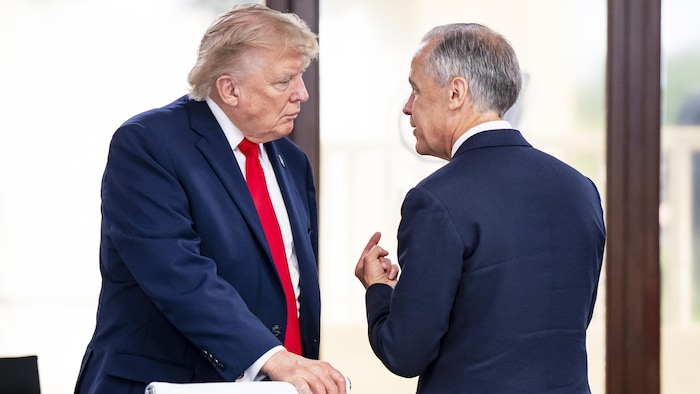 Donald Trump et Mark Carney discutent debout face à face, l'homme de droite faisant un geste de la main.