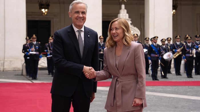 Mark Carney et Giorgia Meloni se serrent la main sur un tapis rouge.