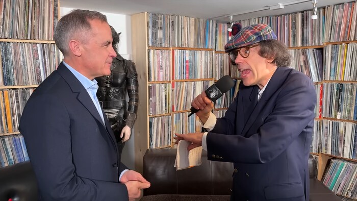 Mark Carney se fait interviewer par Nardwuar dans une salle remplie de vinyles.