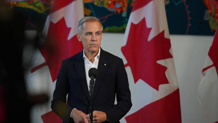 Mark Carney en constituent   de presse devant des drapeaux du Canada.