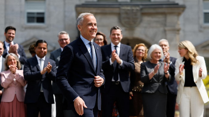 Le premier ministre canadien Mark Carney arrive pour une conférence de presse, tandis que les membres du nouveau cabinet se tiennent derrière lui, à l'extérieur de Rideau Hall.